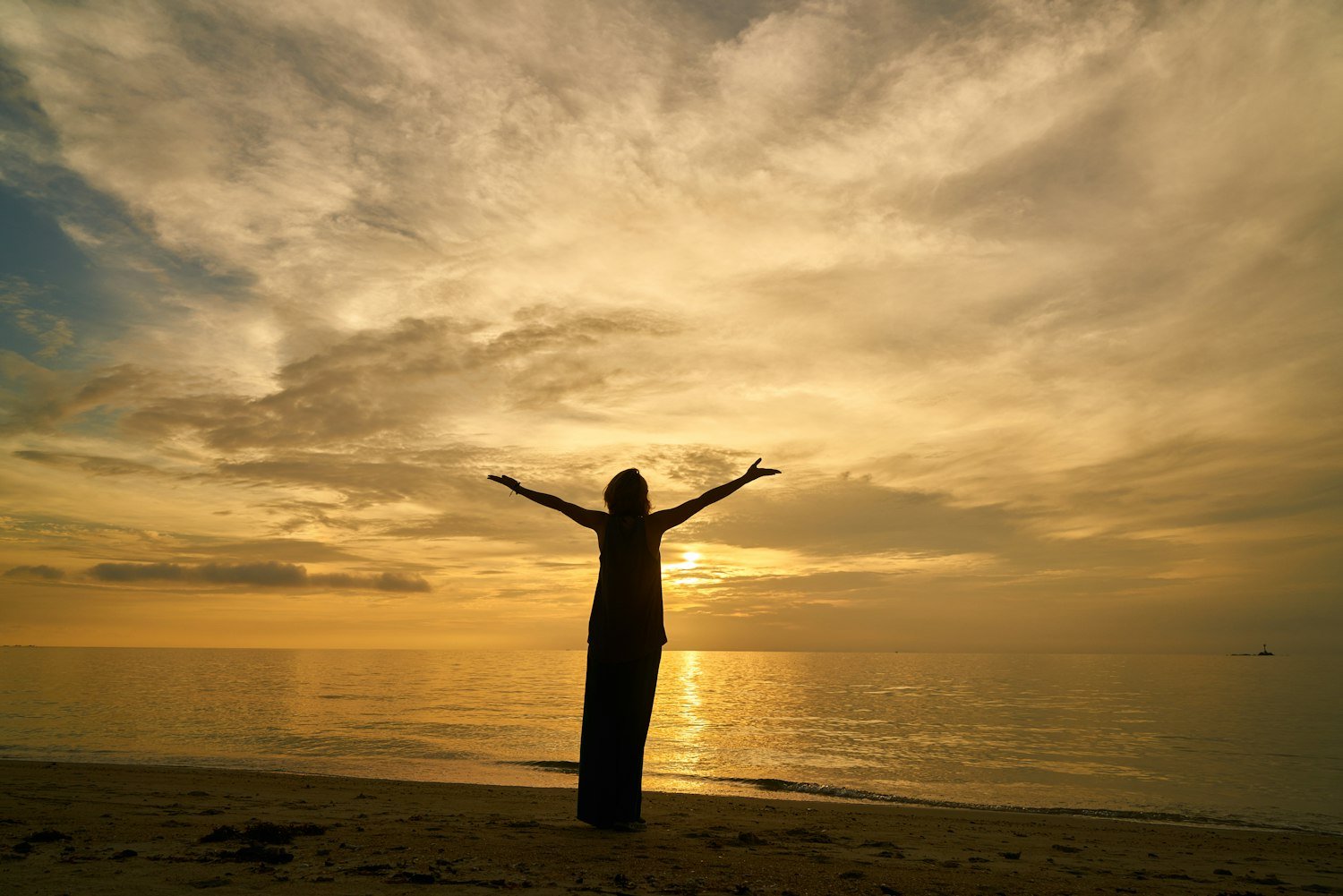 A woman standing on the shore at sunrise with her arms thrown open to the sky